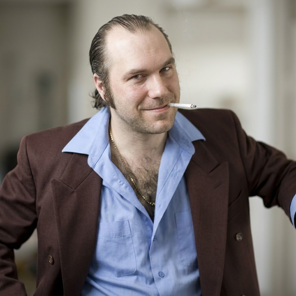 Sales Guy Sam, leaning on something, smiling, cigarette unlit